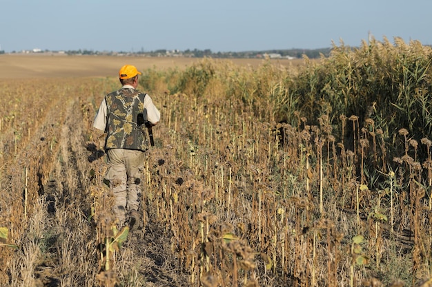 Duck hunter with shotgun walking through a meadow xarear view\
of a man with a weapon in his hands