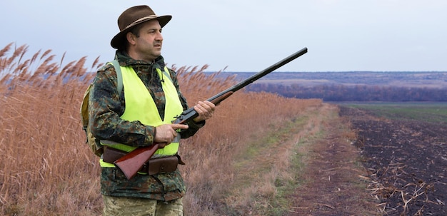 Duck hunter with shotgun walking through a meadow