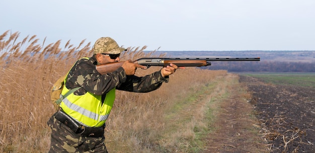 Duck hunter with shotgun walking through a meadow