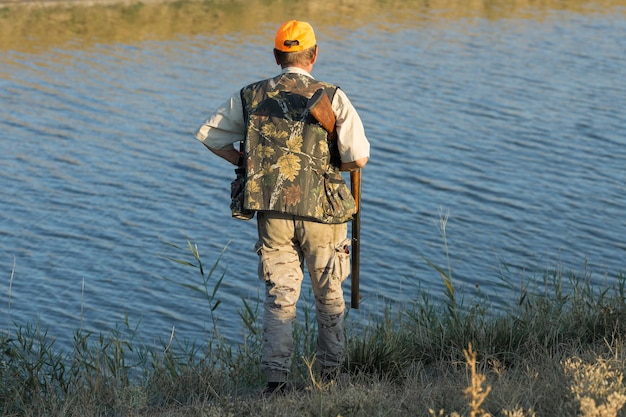 Duck hunter with shotgun walking through a meadow