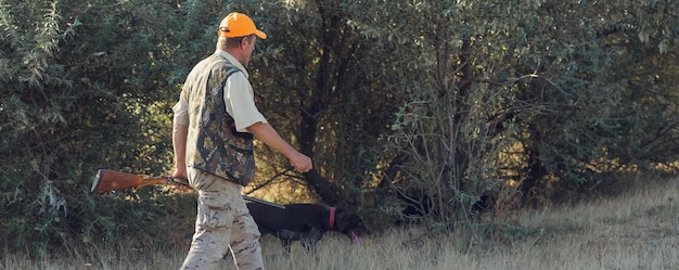 Duck hunter with shotgun walking through a meadow