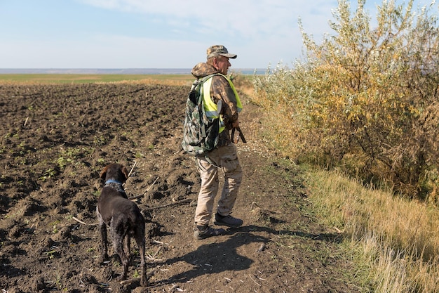 Duck hunter with shotgun walking through a meadow