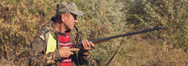 Duck hunter with shotgun walking through a meadow