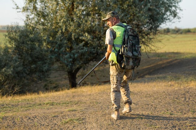 Duck hunter with shotgun walking through a meadow.