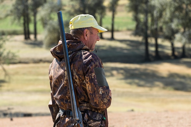 Duck hunter with shotgun walking through a meadow.