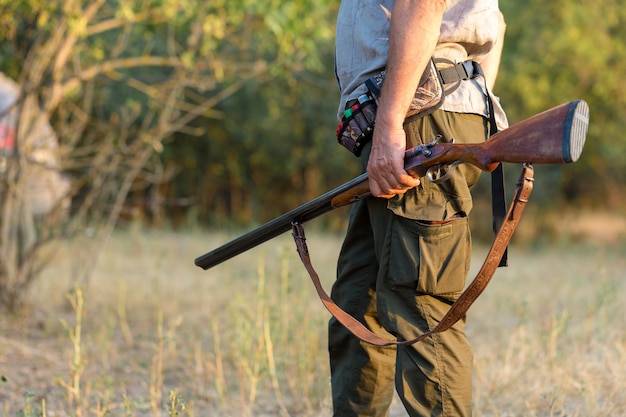 Duck hunter with shotgun walking through a meadow.