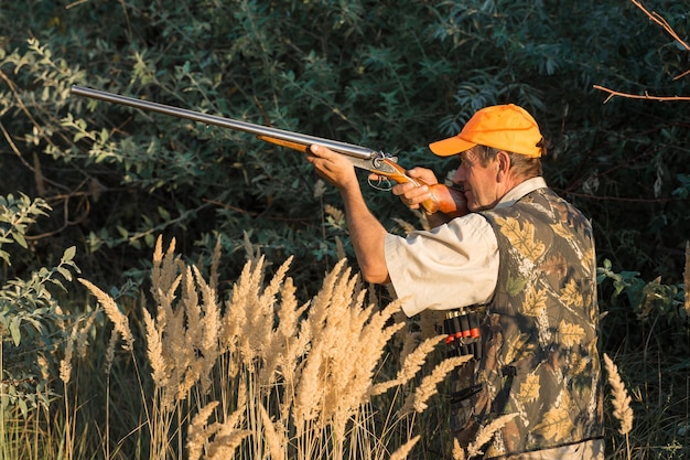 Duck hunter with shotgun walking through a meadow.