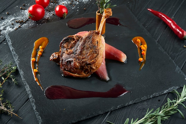 Duck leg confit with caramelized pear on black slate blackboard on black wood