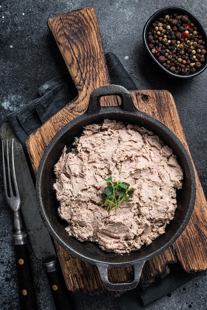 Паштет из утки Rillettes de Canard на сковороде с зеленью. Черный фон. Вид сверху.