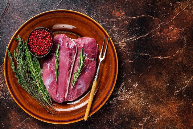 Duck raw breast  steaks on rustic plate with rosemary. Dark background. Top View. Copy space.