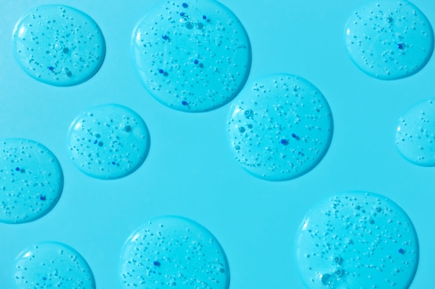 Duidelijke gelreiniger vlekken op blauwe achtergrond. Cosmetische scrubtextuur met blauwe pillingdeeltjes. Schoonheid concept achtergrond