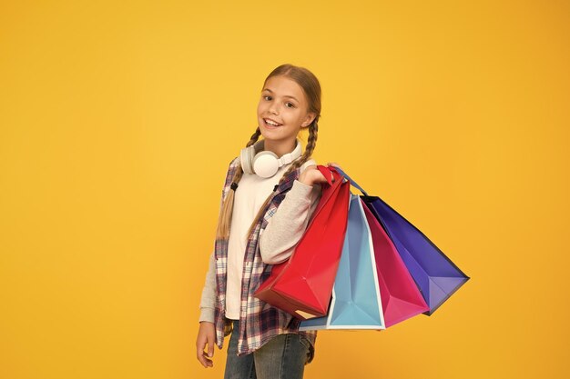 Duik in winkelen Gelukkig kind met papieren zakken Kleine meisjesglimlach met boodschappentassen op gele achtergrond Vakantievoorbereiding en feest Winkelen en verkoop op zwarte vrijdag Verslaafde consument