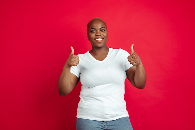 Duim omhoog. Het portret van de Afro-Amerikaanse jonge vrouw op rood. Mooi vrouwelijk model in overhemd.