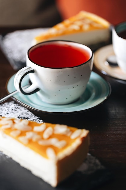 Duindoorn-cheesecake bestrooid met amandelblaadjes? met een kopje fruitthee in een gezellige koffieshop, donkere achtergrond