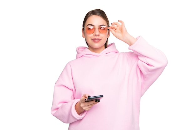 Duizendjarige meisje in casual roze hoodie met smartphone rollende ogen naar boven aanpassen bril geïsoleerd op witte mobiel