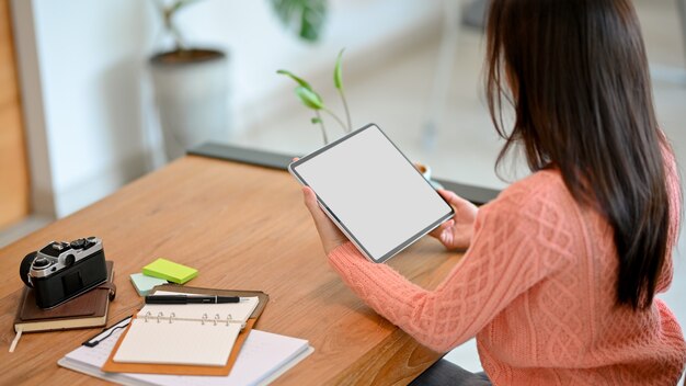 Duizendjarige vrouw in roze trui met werken op zoek naar draagbare digitale tablet