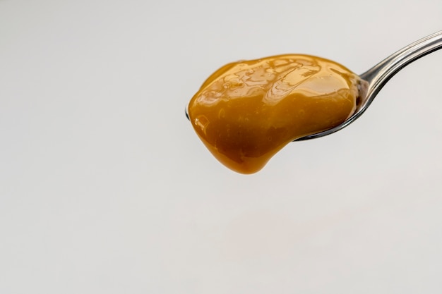 Dulce de leche che gocciola dal cucchiaio, sfondo bianco