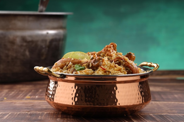 Dum chicken biriyani, close up image of Kerala-Thalassery biriyani  which is mixed with masala  and garnished with lemon  slices ,arranged in a copper serving bowl  placed on wooden table with big coo