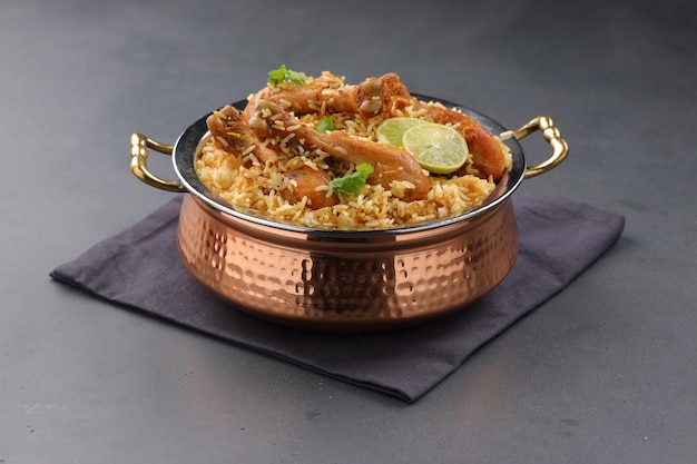 Dum chicken biriyani, close up image of Kerala-Thalassery biriyani  which is mixed with masala and yellow in colour arranged in a copper serving bowl and garnished with lemon slices  placed on graphit