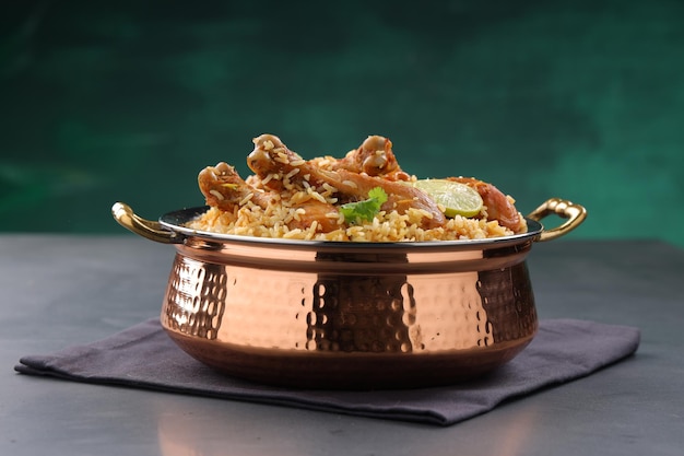 Dum chicken biriyani, close up image of Kerala-Thalassery biriyani  which is mixed with masala and yellow in colour arranged in a copper serving bowl and garnished with lemon slices  placed on graphit