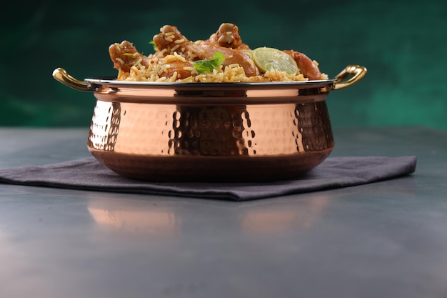 Dum chicken biriyani, close up image of Kerala-Thalassery biriyani  which is mixed with masala and yellow in colour arranged in a copper serving bowl and garnished with lemon slices  placed on graphit