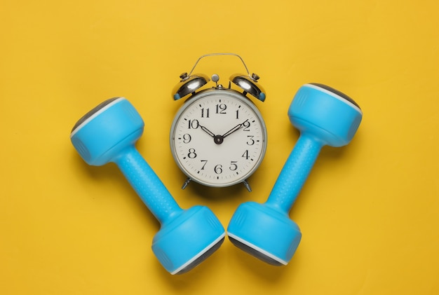 Dumbbell, alarm clock on yellow