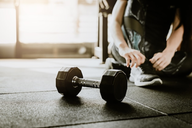 Dumbbell on the floor in gym with woman tying her shoelaces in background