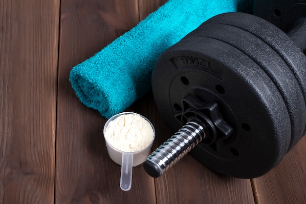 Dumbbell and supplements on wooden floor. fitness background with blue towel.