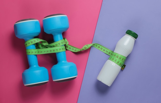 Dumbbells, bottle of kefir, measuring tape on colored paper