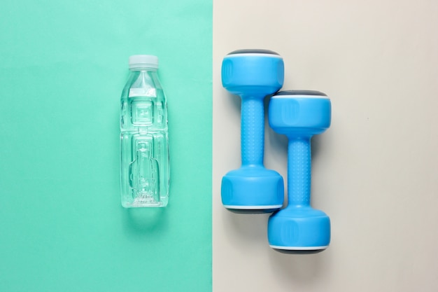  Dumbbells, bottle of water on colored surface. 