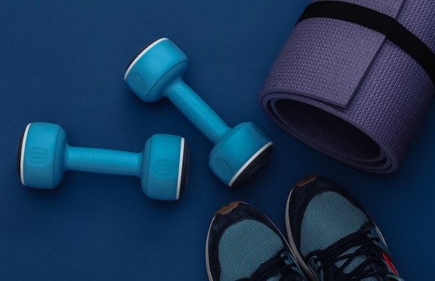 Dumbbells, fitness mat and sneakers on classic blue background. Healthy lifestyle, fitness training. Color 2020. Top view. Flat lay