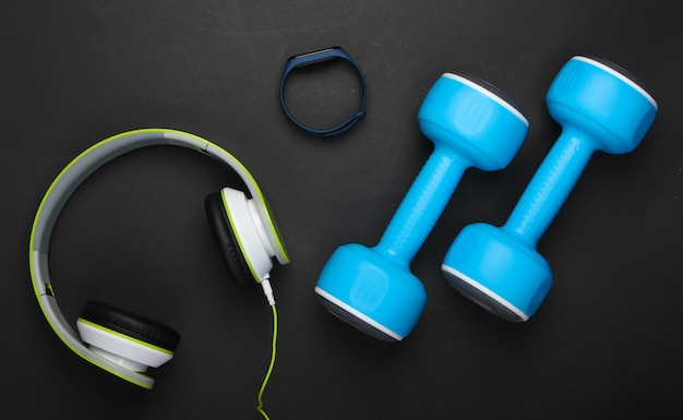 Dumbbells, headphones, smart bracelet, wate on black surface