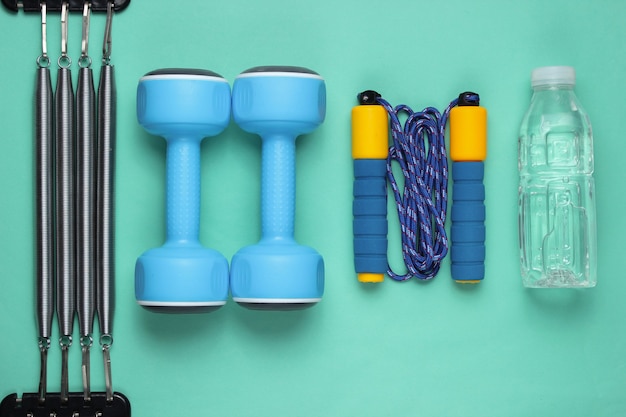 Dumbbells, jump rope, bottle of water, expander. Sports equipment on blue background. Top view