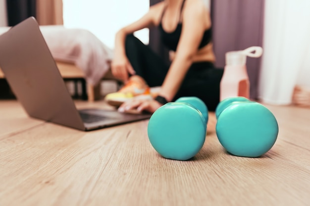 Dumbbells lie on the floor, against the background of a young woman with a laptop