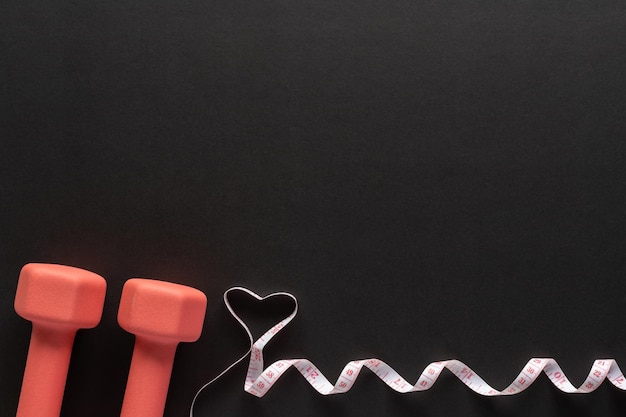 Dumbbells and measuring tape on black background fitness sport and workout concept flat lay