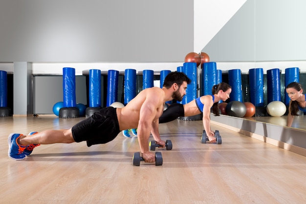 Dumbbells push-ups couple at fitness gym 