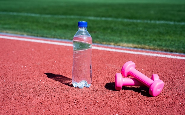 Dumbbells on racetrack in stadium hydration after fitness healthy balanced lifestyle maintain water balance in body while training barbells and bottle on running track sport tool and equipment