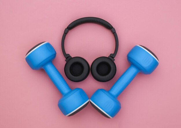 Dumbbells and stereo headphones on pink background. Sport concept. Top view