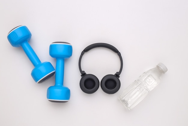 Dumbbells and stereo headphones, water bottle on white background. Sport and fitness concept. Top view