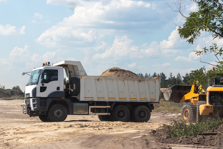 Dump truck with bunch of land in the back and excavator at the construction site outside the city