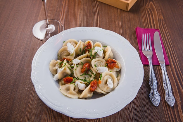 Photo dumplings bowl with herbs tomatoes and sour cream on a brown table background in restaurant