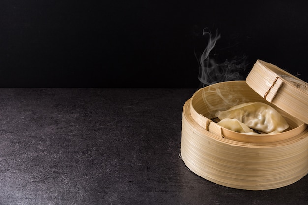 Dumplings or gyoza served in traditional steamer on black background. 