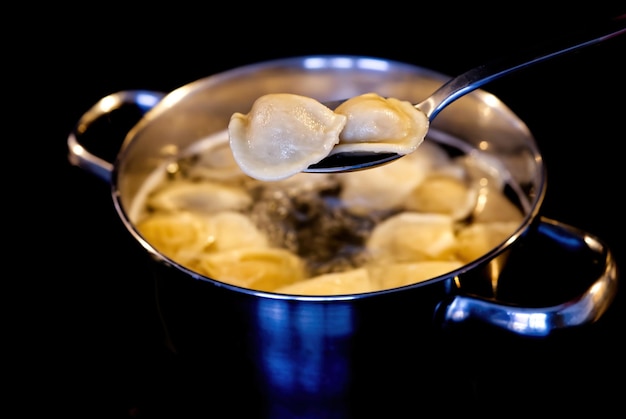 Dumplings mixed with a spoon in a pot of boiling water Boiled dumplings in a pan black background