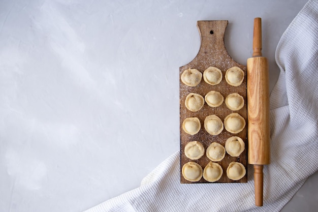 Dumplings op snijplank met deegroller en wafel witte handdoek op grijze achtergrond voor tekst