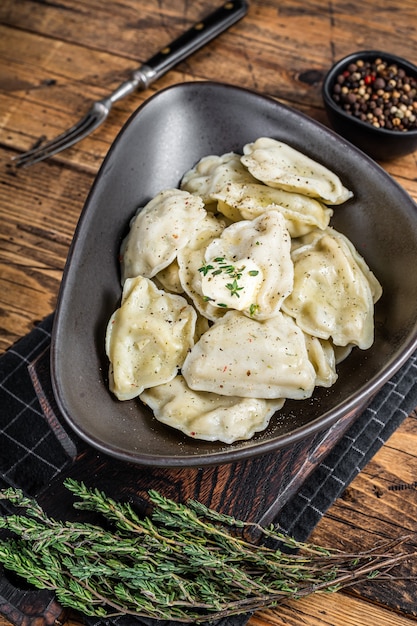 Dumplings pierogi met aardappel in een bord met kruiden en boter. Houten tafel. Bovenaanzicht.