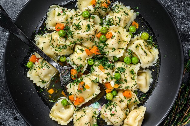 Zuppa di gnocchi con ravioli in una ciotola con verdure. sfondo nero. vista dall'alto.