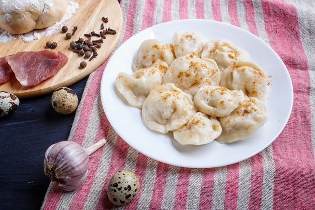 Dumplings with ingredients (meat, dough, spices) on a linen tablecloth