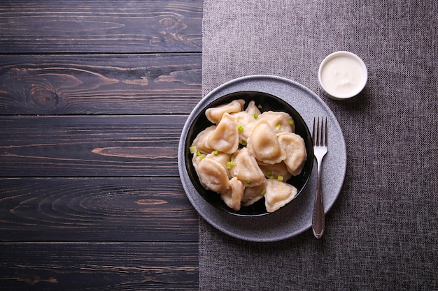 Dumplings with potatoes and sour cream on a wooden background with place for text. Vareniki is a dish of Slavic cuisine.