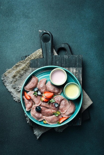 Dumplings with strawberries and sour cream On a black stone background In a plate closeup