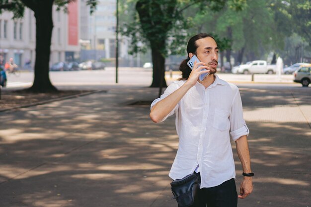 Dunne jonge Latijns-man praten op mobiele telefoon tijdens het wandelen in de stad Kopieer de ruimte